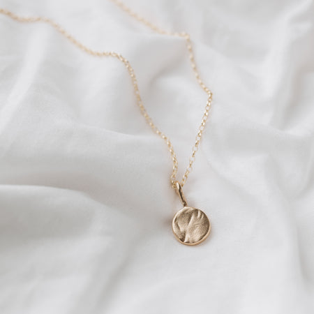 A 9ct gold full moon-shaped pendant necklace laid out on a white fabric surface.