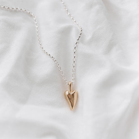 A 9ct gold heart-shaped pendant necklace laid out on a white surface.