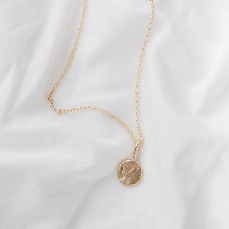 A 9ct gold full moon-shaped pendant necklace laid out on a white fabric surface.