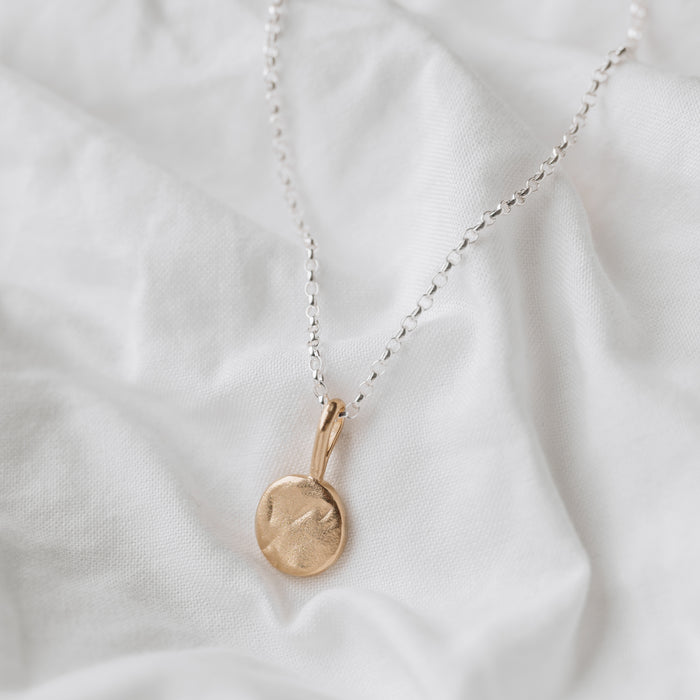 A 9ct gold moon-shaped pendant necklace laid out on a white fabric surface.