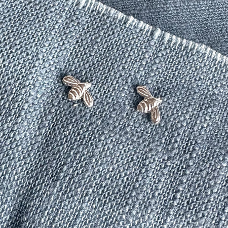 Two silver bee-shaped earrings on a denim background