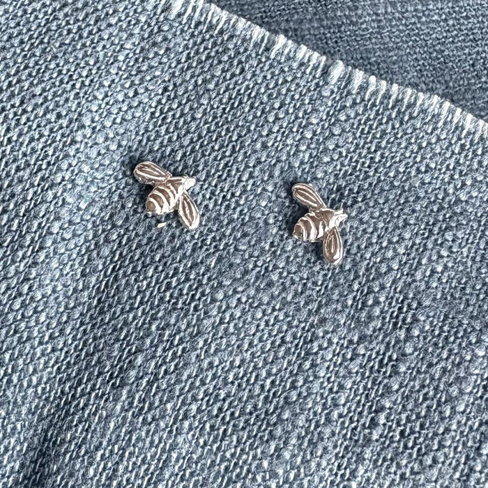 Two silver bee-shaped earrings on a denim background
