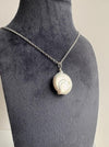 Necklace with a large coin pearl pendant on a navy mannequin bust.