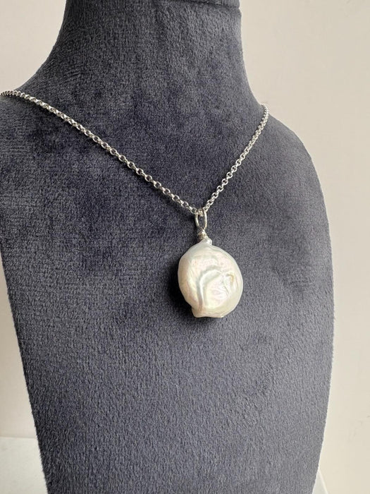 Necklace with a large coin pearl pendant on a navy mannequin bust.