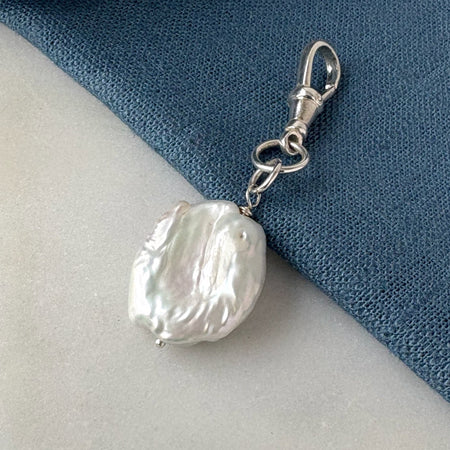 Pearl charm with silver clasp on a blue and white fabric background