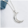 A silver crescent moon pendant attached to a chunky belcher chain, displayed against a white background