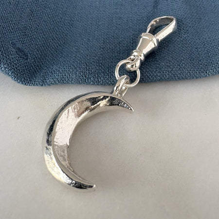 Silver crescent moon charm on a blue fabric background