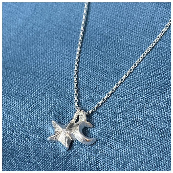 A silver pendant featuring a crescent moon and a small guiding star, hanging from a silver chain on a blue textured background.