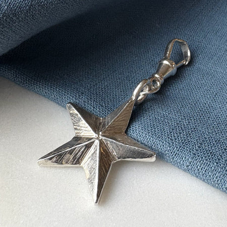 Silver star-shaped pendant on a blue fabric background