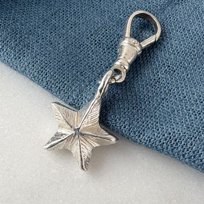 Silver star-shaped charm on a blue and white fabric background