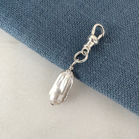 Silver charm with a pearl-like bead on a blue and white background
