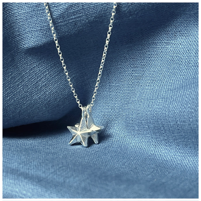 A silver pendant featuring two guiding stars charms attached to a small chain, displayed against a blue background.