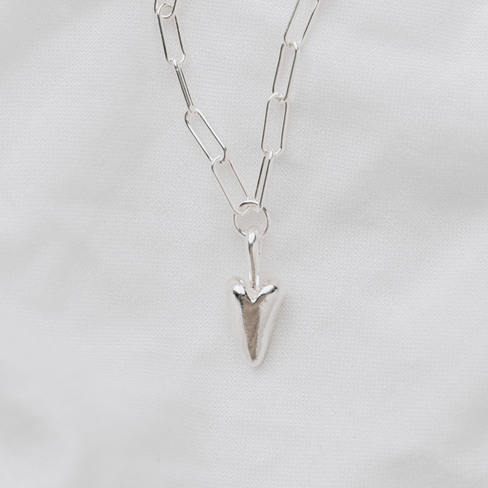 A chunky silver heart hanging from a silver trace chain necklace