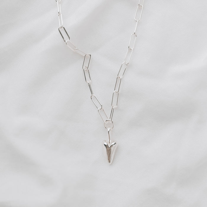 A chunky silver heart hanging from a silver trace chain necklace
