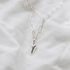 A silver trace chain necklace with a heart-shaped pendant, displayed on a textured white background.