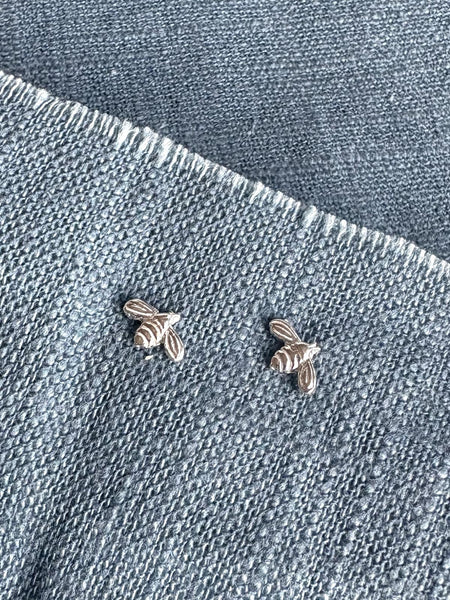 Two silver bee-shaped earrings on a denim background