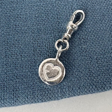 Silver charm with a heart design on a blue textured background