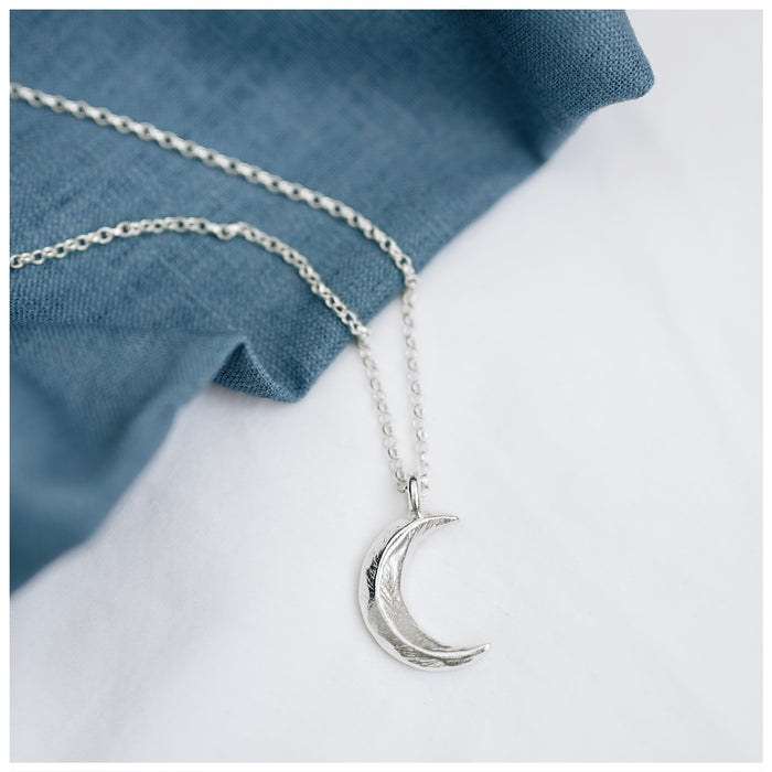 A silver crescent moon pendant attached to a chunky belcher chain, displayed against a white background