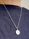 Silver necklace with a large coin pearl on a female wearing a dark blue shirt.