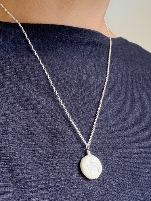 Silver necklace with a large coin pearl on a female wearing a dark blue shirt.