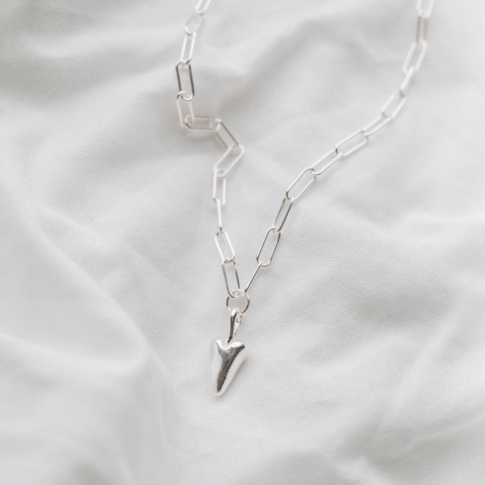 A chunky silver heart hanging from a silver trace chain necklace