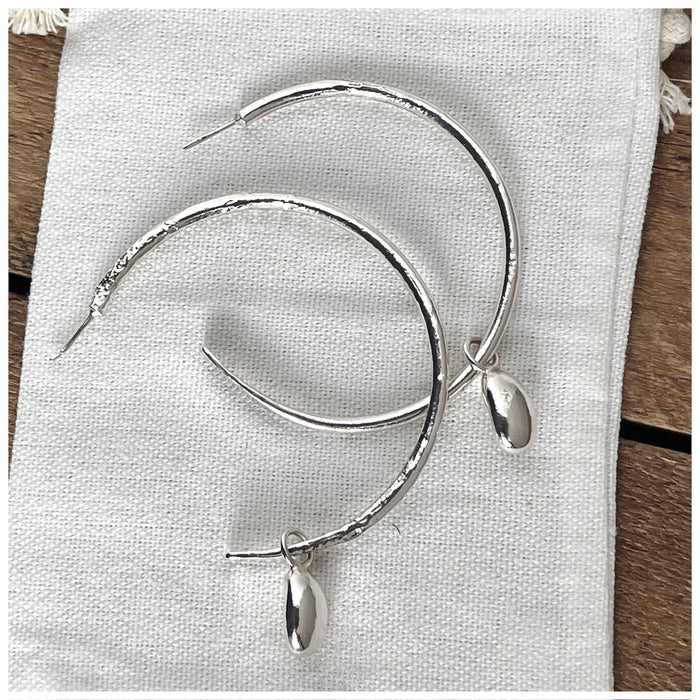 A pair of silver maxi globed hooped earrings with two large pebbles hanging from each hoop, displayed on a wooden surface.