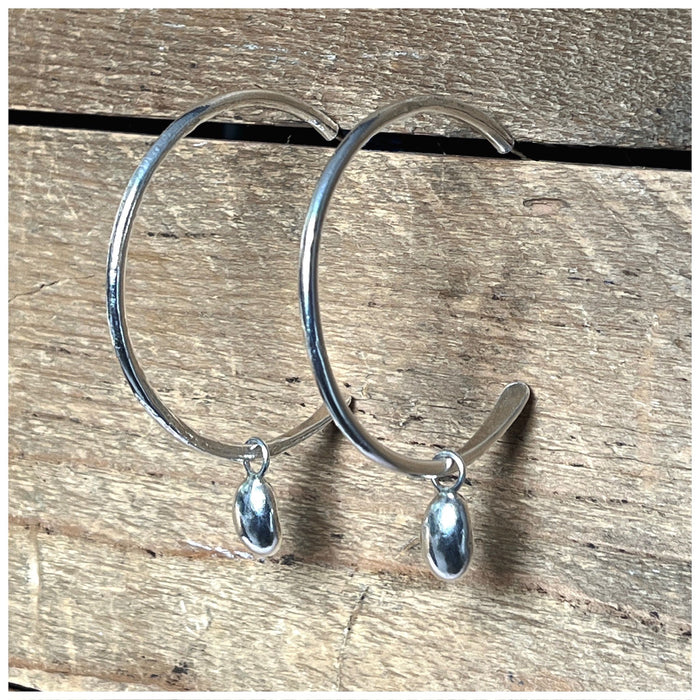 A pair of silver maxi globed hooped earrings with two large pebbles hanging from each hoop, displayed on a wooden surface.