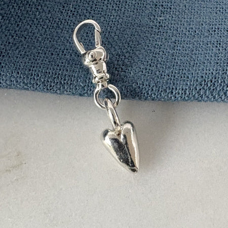 Silver charm shaped like a heart on a blue and gray background