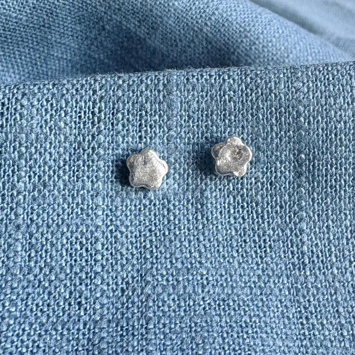 Silver mini flower shaped silver earrings on a blue textured fabric background