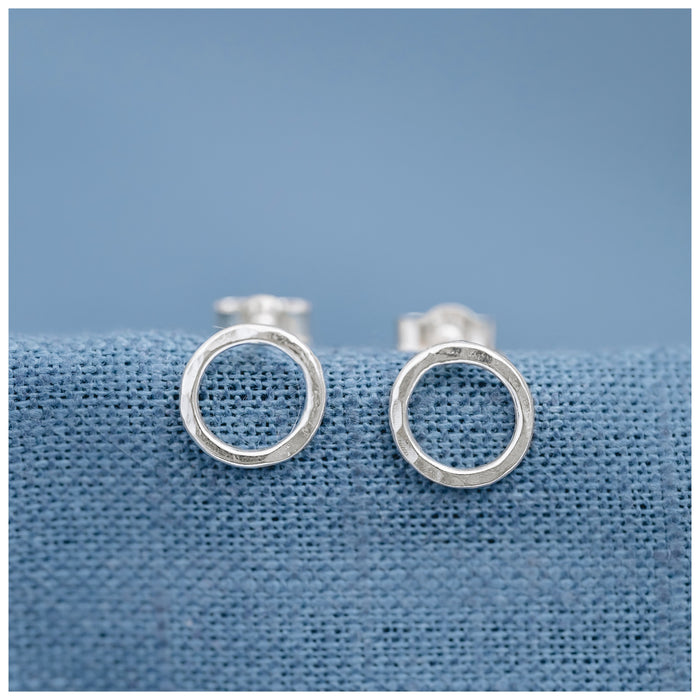 Mini halo or circle stud earrings on a light blue linen background