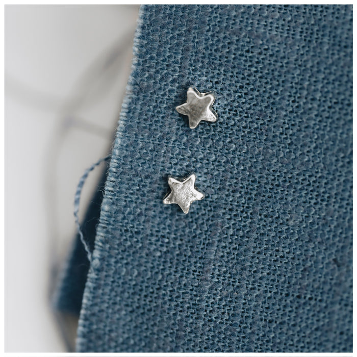 Miniature star stud earrings on a blue linen background