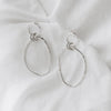 Organically shaped double hooped dangly earrings on a plain white linen background.