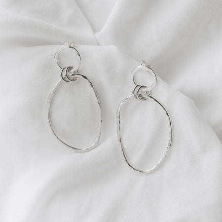 Organically shaped double hooped dangly earrings on a plain white linen background.