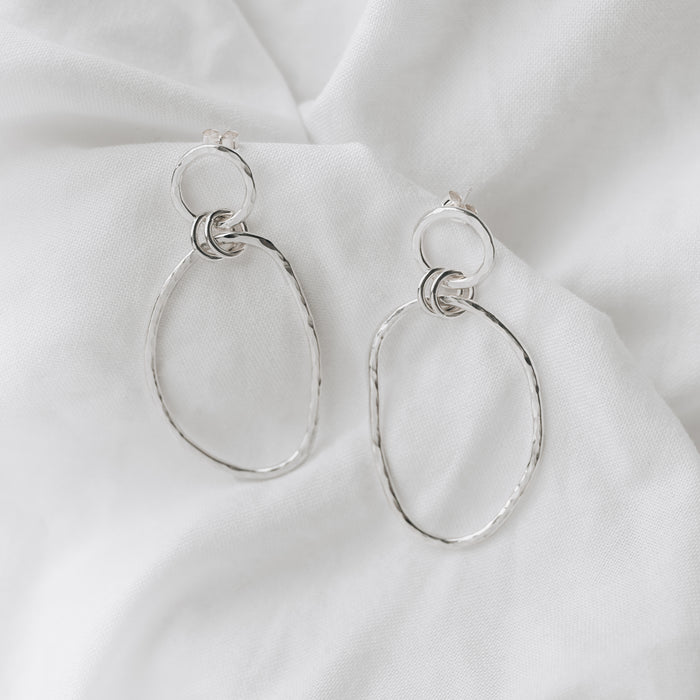 Organically shaped double hooped dangly earrings on a plain white linen background.