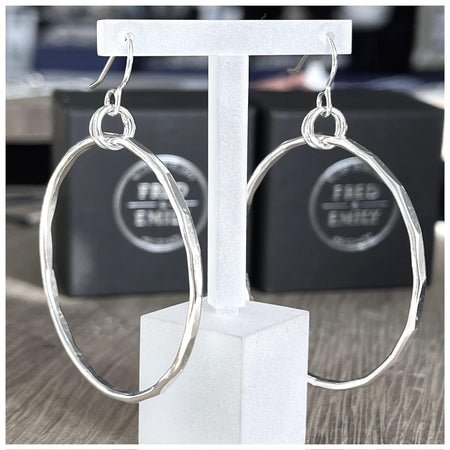 A pair of sterling silver hoop earrings with a hammered effect, displayed on a clear t bar earring holder