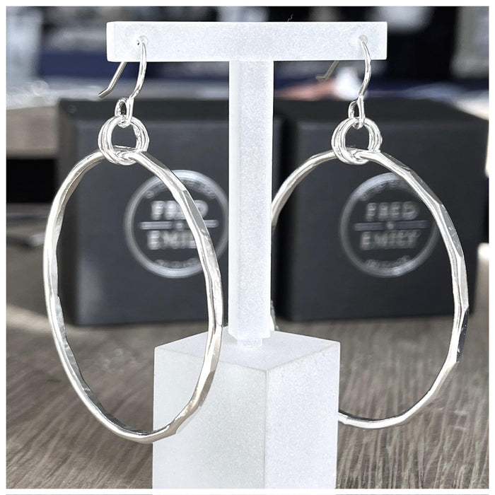 A pair of sterling silver hoop earrings with a hammered effect, displayed on a clear t bar earring holder