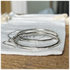 A pair of sterling silver hoop earrings with a hammered effect, displayed on a textured wooden surface and white linen bag