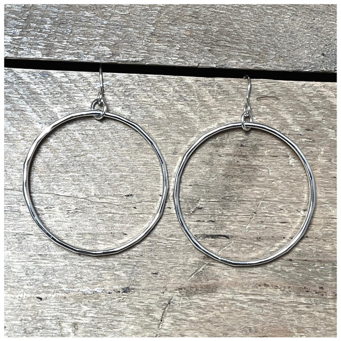 A pair of sterling silver hoop earrings with a hammered effect, displayed on a textured wooden surface.