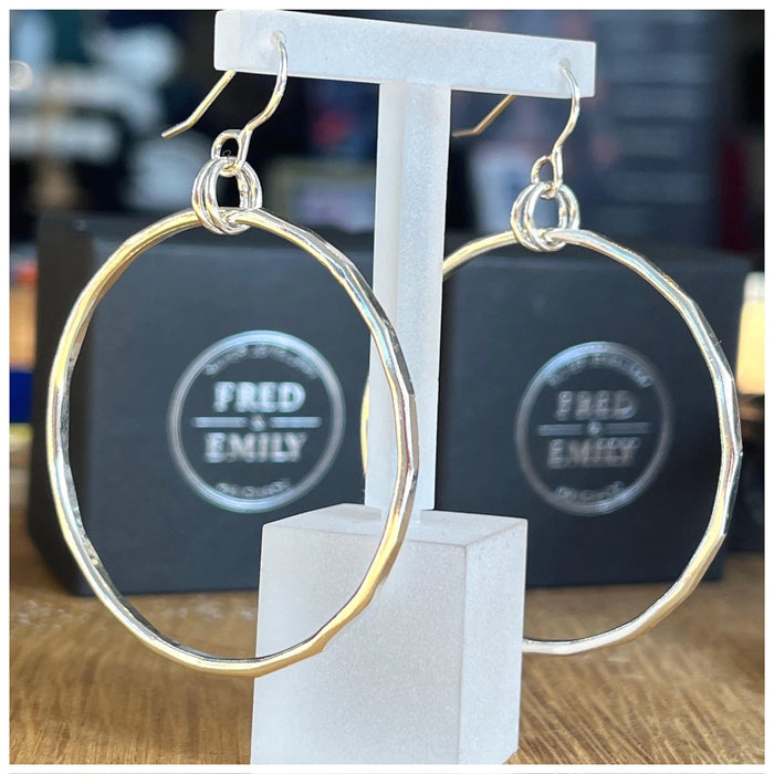 A pair of sterling silver hoop earrings with a hammered effect, displayed on clear t bar display.