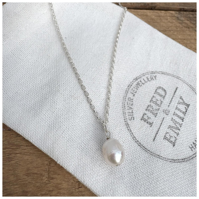 A silver pearl pendant hanging from a sterling silver belcher chain, displayed on a white fabric with a Fred & Emily stamp.