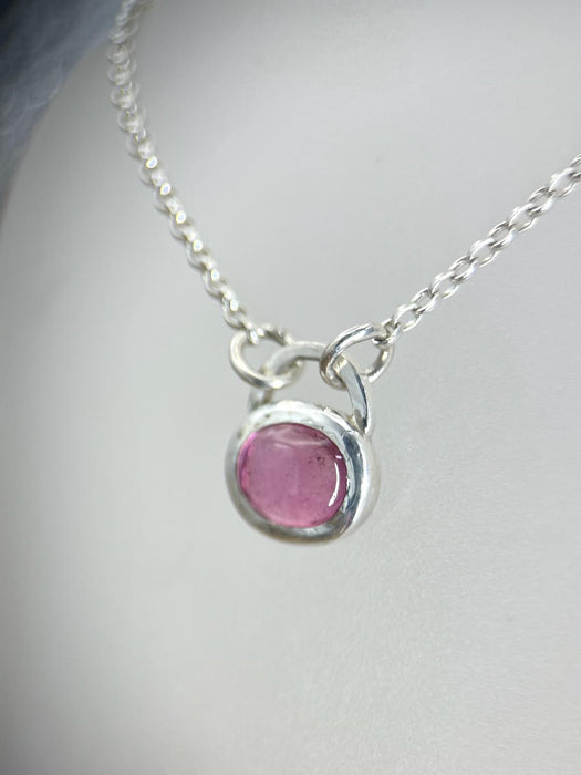 A sterling silver pendant with an oval pink tourmaline stone on an 18'' belcher chain.