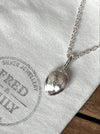A steriing silver pendant shaped like a pumpkin seed hanging on a chunky chain on a linen bag