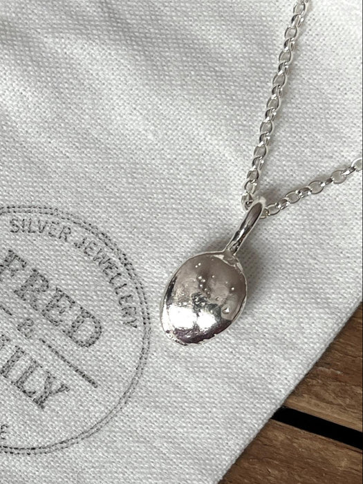 A steriing silver pendant shaped like a pumpkin seed hanging on a chunky chain on a linen bag