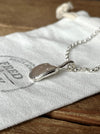 A silver pendant in the shape of a pumpkin seed, attached to a 2.5mm belcher chain, displayed on a white fabric pouch with the brand 'Fred & Emily' stamped on it.