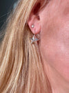 A close-up of a person's ear wearing a silver dangling star earring and a small silver stud earring, with blonde hair framing the side of the face.