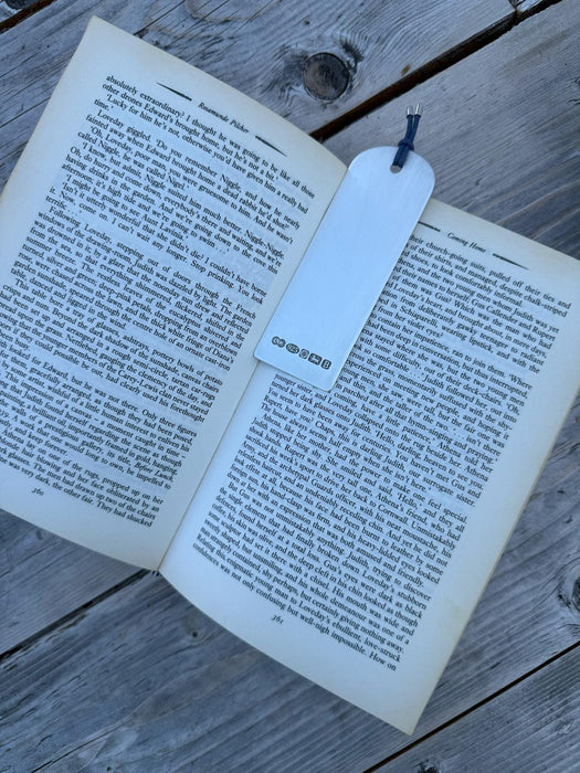 A sterling silver bookmark with a blue ribbon tail rests on an open book spread on a weathered gray wooden surface.