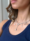 Woman wearing a silver charm necklace with various charms against a neutral background