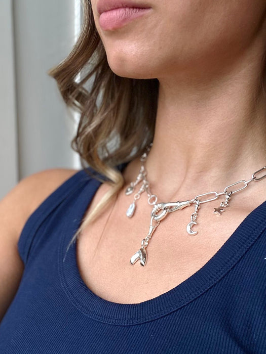 Woman wearing a silver charm necklace with various charms against a neutral background