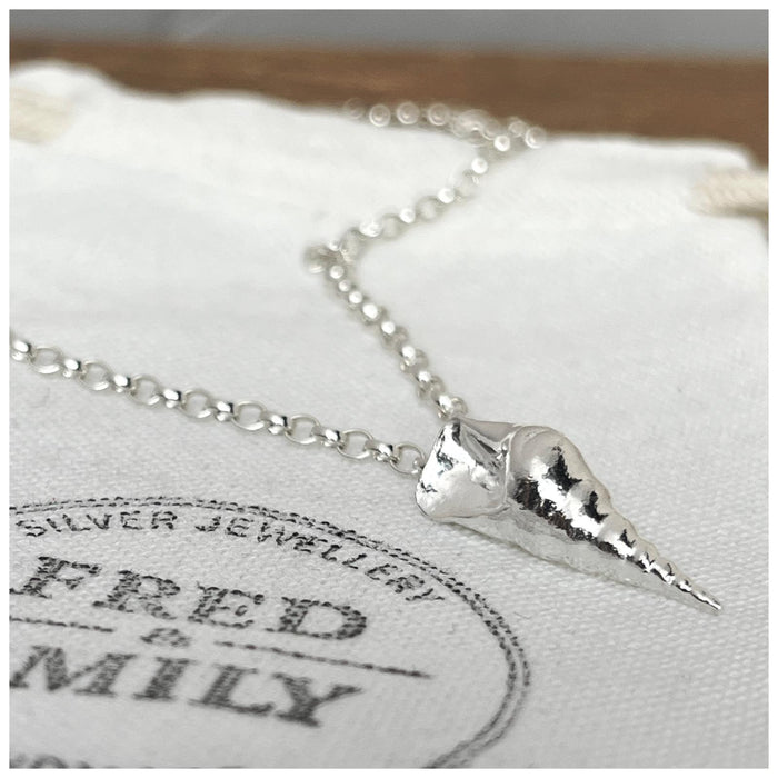 A sterling silver conch sea shell pendant hanging on a 2.5mm belcher chain, displayed against a white background with a Fred & Emily Stamp