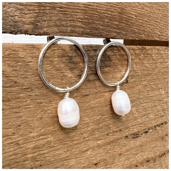 A pair of silver hoop earrings with freshwater pearl drops, displayed against a wooden background.